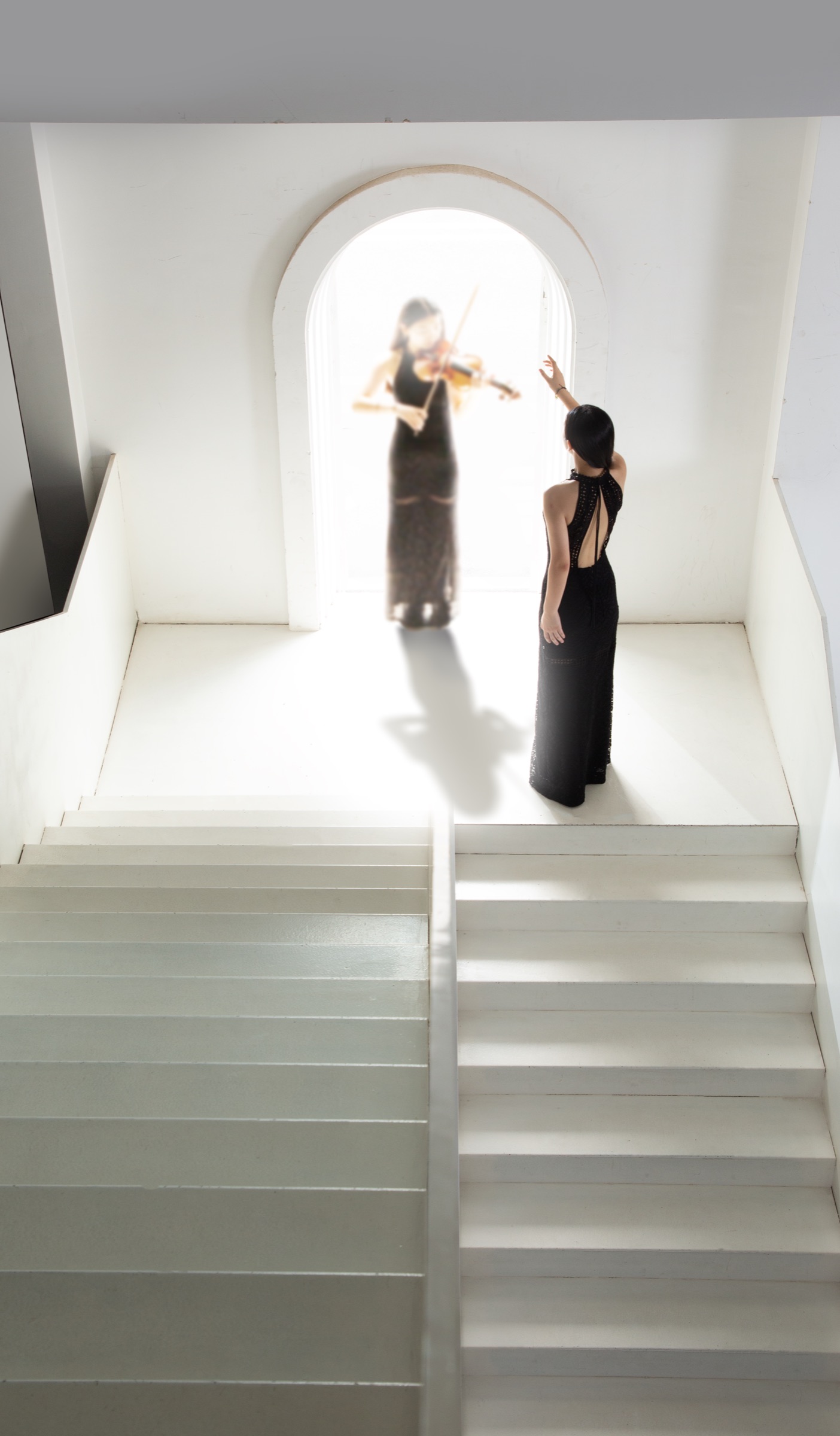 At the top of the stairs, Calina in black reaches up toward the violinist in the arch.
